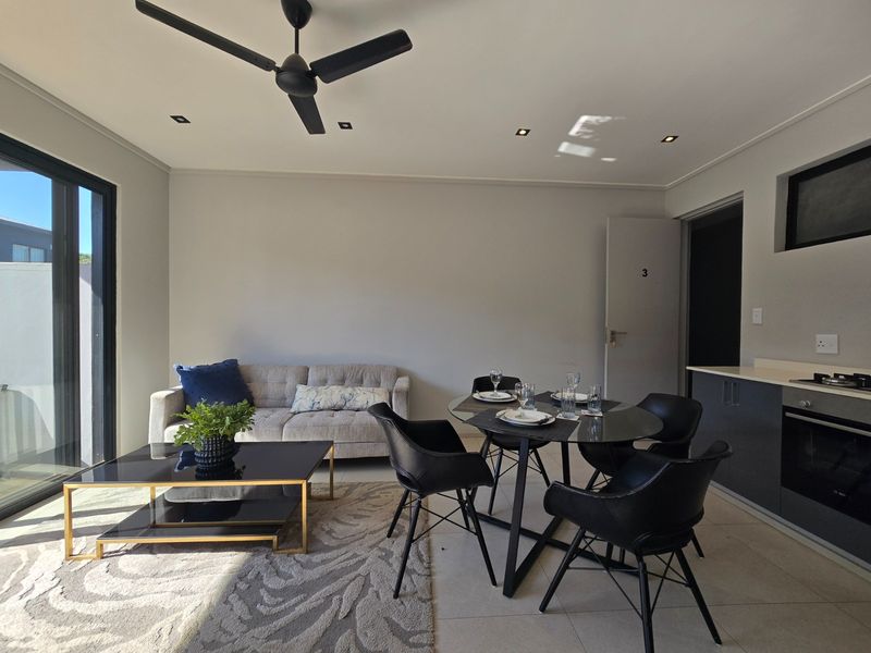 Modern open-plan living and dining area featuring a sleek kitchen with built-in appliances, recessed lighting, and direct access to an outdoor space.