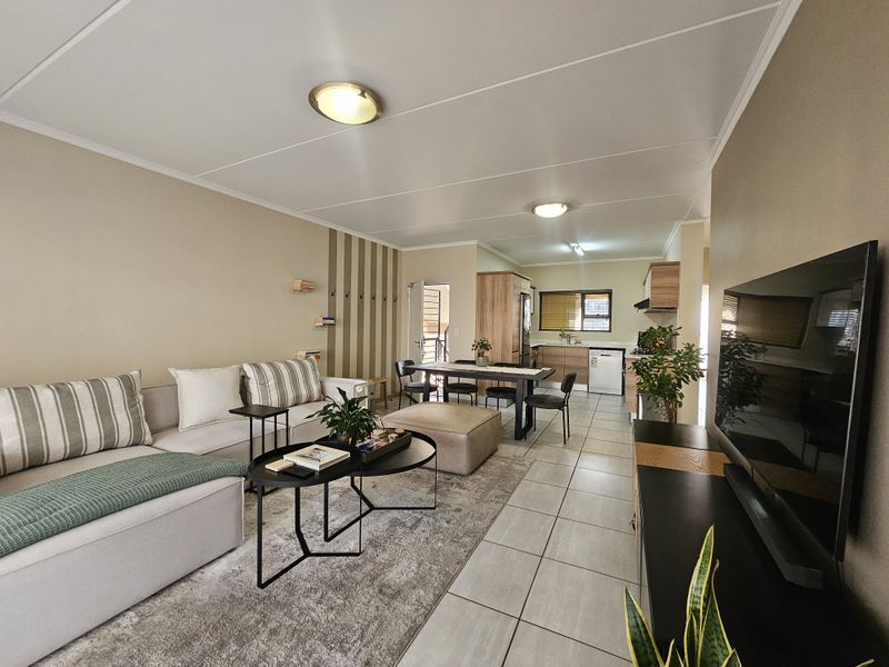 An open-plan living and kitchen area featuring tiled flooring, neutral wall tones, and functional built-in cabinetry, creating a cohesive and well-lit living space.
