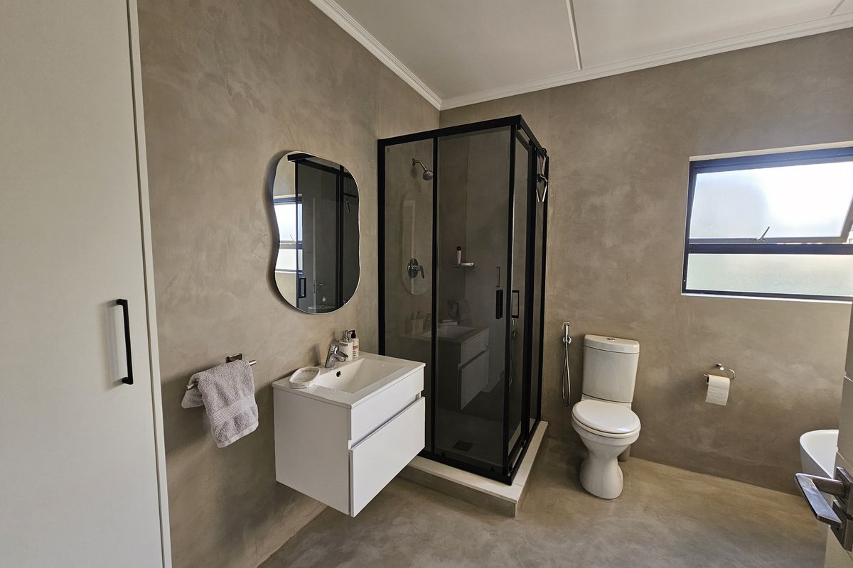 Modern bathroom featuring a sleek wall-mounted vanity, a black-framed shower enclosure, and contemporary concrete-look wall finishes.