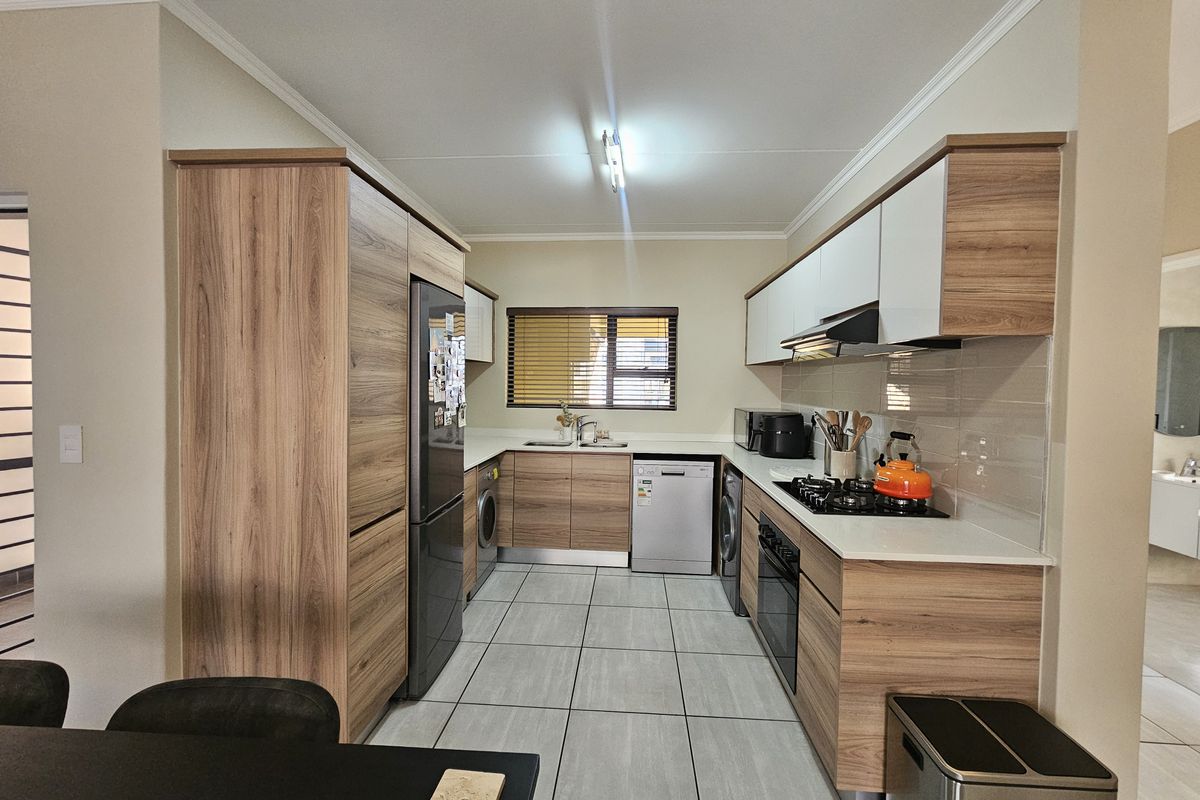 Modern kitchen featuring wood-grain cabinetry, gas hob, integrated oven, extractor fan, and tiled flooring with a functional layout.