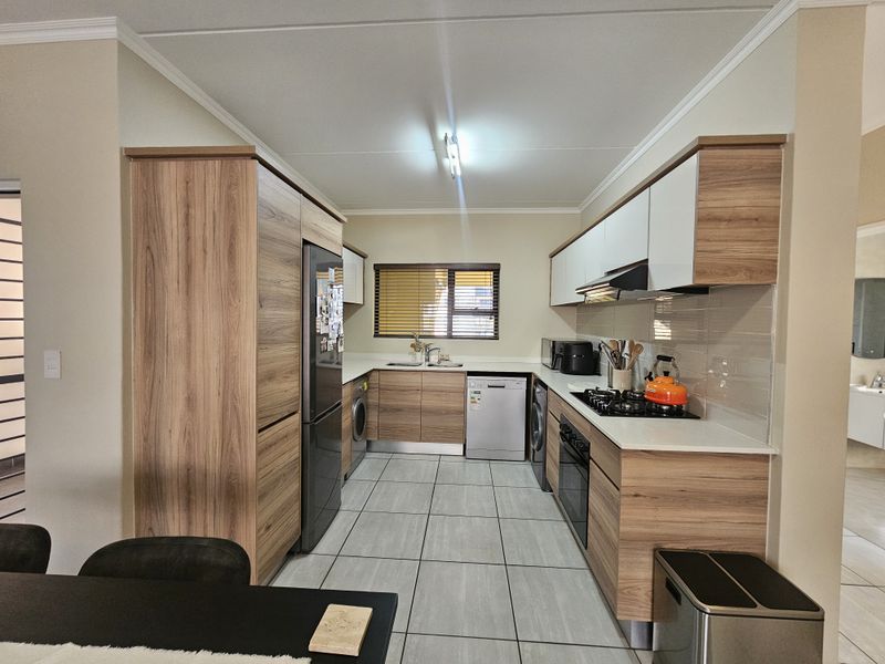 Modern kitchen featuring wood-grain cabinetry, gas hob, integrated oven, extractor fan, and tiled flooring with a functional layout.