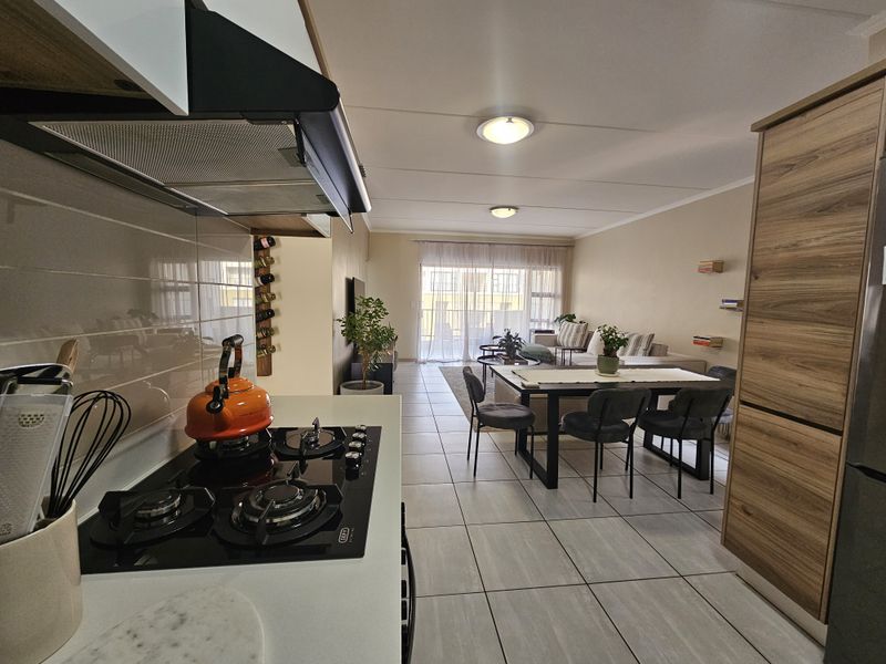 Modern open-plan living area featuring a well-equipped kitchen with gas hob, tiled flooring, and seamless flow to a bright lounge with sliding door access.