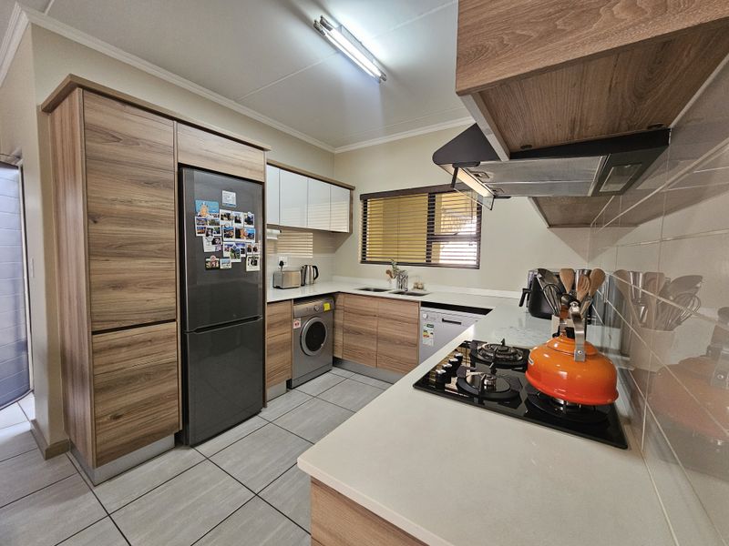 Modern kitchen featuring wood-finish cabinetry, stone countertops, a gas hob with extractor fan, and integrated laundry and dishwasher appliances.