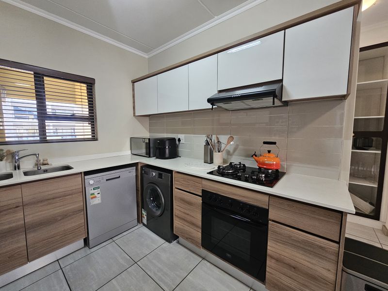 Modern kitchen featuring wood-grain and white cabinetry, stone countertops, gas hob, built-in oven, extractor fan, and tiled backsplash.