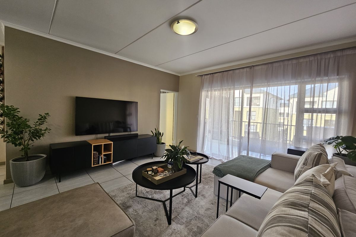A well-lit living room featuring tiled flooring and a large sliding glass door that provides access to an outdoor balcony area.