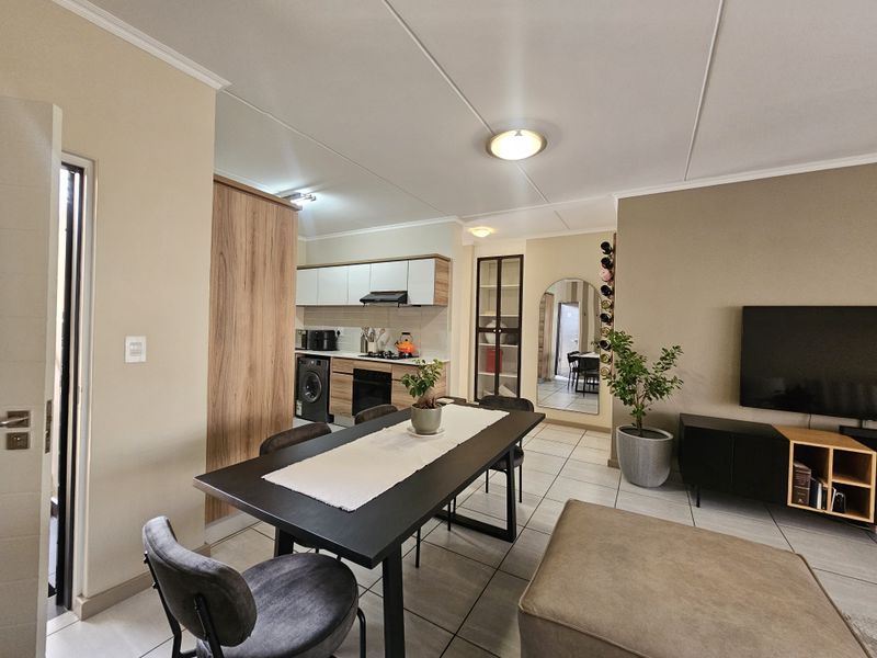A well-maintained open-plan living and dining area featuring a modern kitchen with built-in cabinetry, oven, and hob, complemented by neutral tiled flooring.