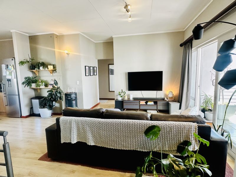 An open-plan living area featuring light laminate flooring, neutral walls, and a large sliding glass door providing access to an outdoor space.