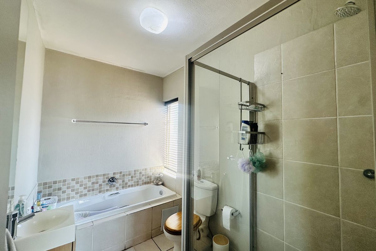 A functional bathroom featuring a built-in bathtub, a separate glass-enclosed shower, a vanity basin, and a toilet with neutral tiled finishes.