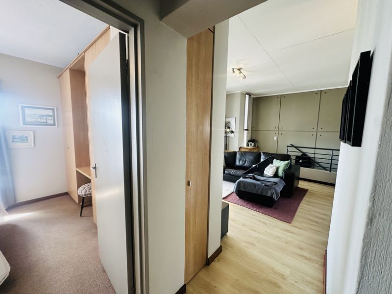 A view from the hallway looking into a bedroom with built-in cabinetry and an open-plan living area featuring laminate flooring and a staircase.