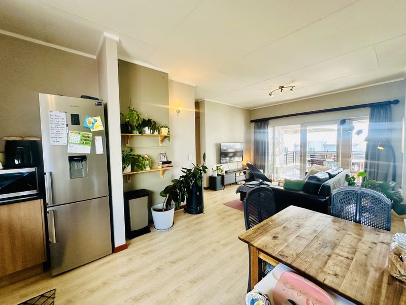 Open-plan living and dining area featuring light laminate flooring, built-in shelving, and large sliding glass doors leading to an outdoor balcony.