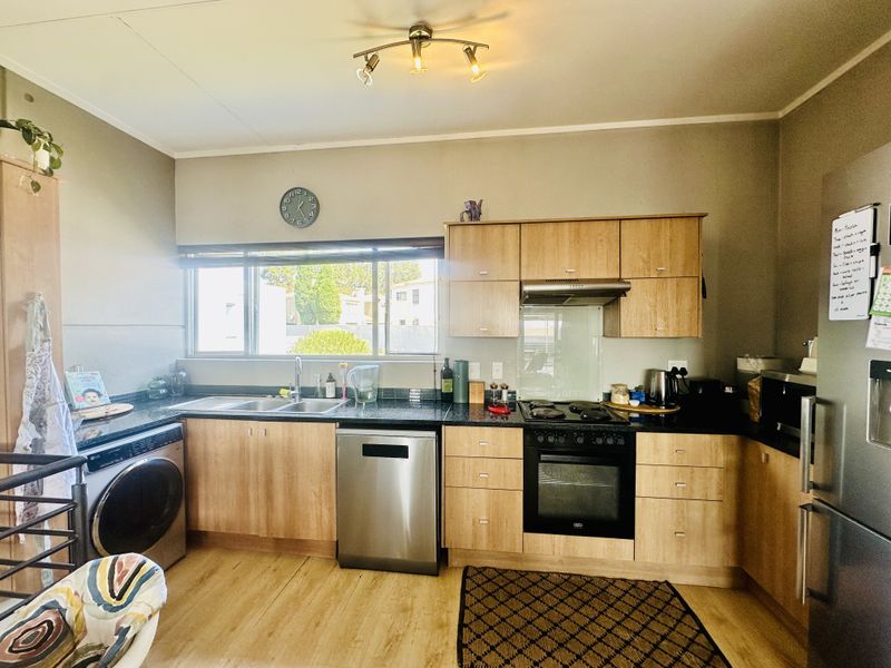 A functional kitchen featuring light wood cabinetry, dark laminate countertops, built-in oven with extractor fan, and integrated dishwasher.