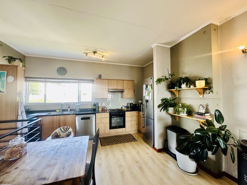 A functional kitchen featuring light wood cabinetry, dark laminate countertops, integrated oven, extractor fan, and durable laminate flooring.