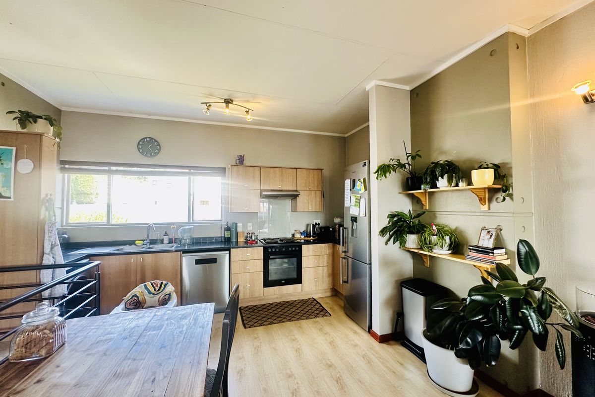A functional kitchen featuring light wood cabinetry, dark laminate countertops, integrated oven, extractor fan, and durable laminate flooring.