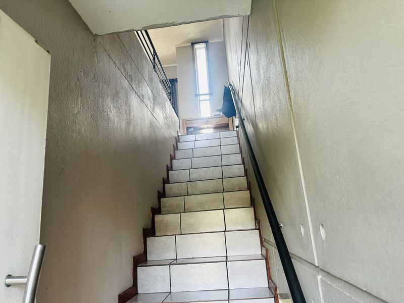 A staircase with tiled steps and a metal handrail leading to an upper level, featuring neutral wall finishes and a vertical window.