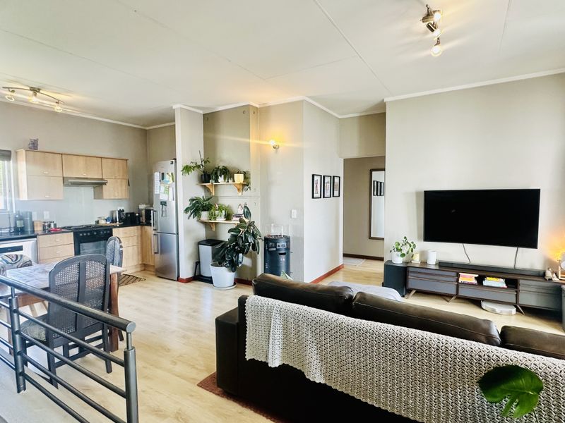 Open-plan living area featuring a functional kitchen with built-in cabinetry and appliances, flowing into a comfortable lounge space with laminate flooring throughout.