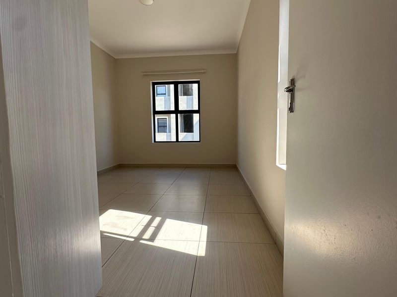 A bright, empty bedroom featuring neutral tiled flooring and a window, providing a clean and versatile space ready for furnishing.