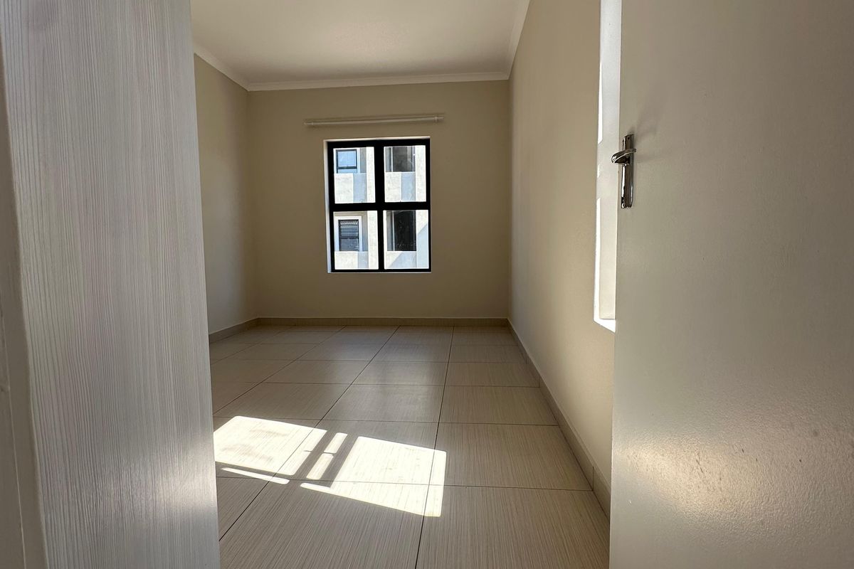 A bright, empty bedroom featuring neutral tiled flooring and a window, providing a clean and versatile space ready for furnishing.