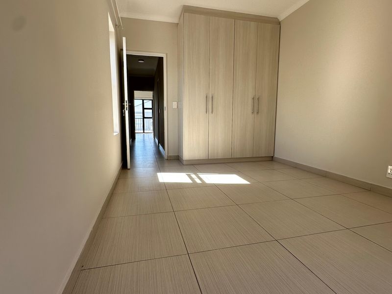 A bright, empty bedroom featuring neutral tiled flooring and modern built-in cupboards, offering a clean and versatile space.