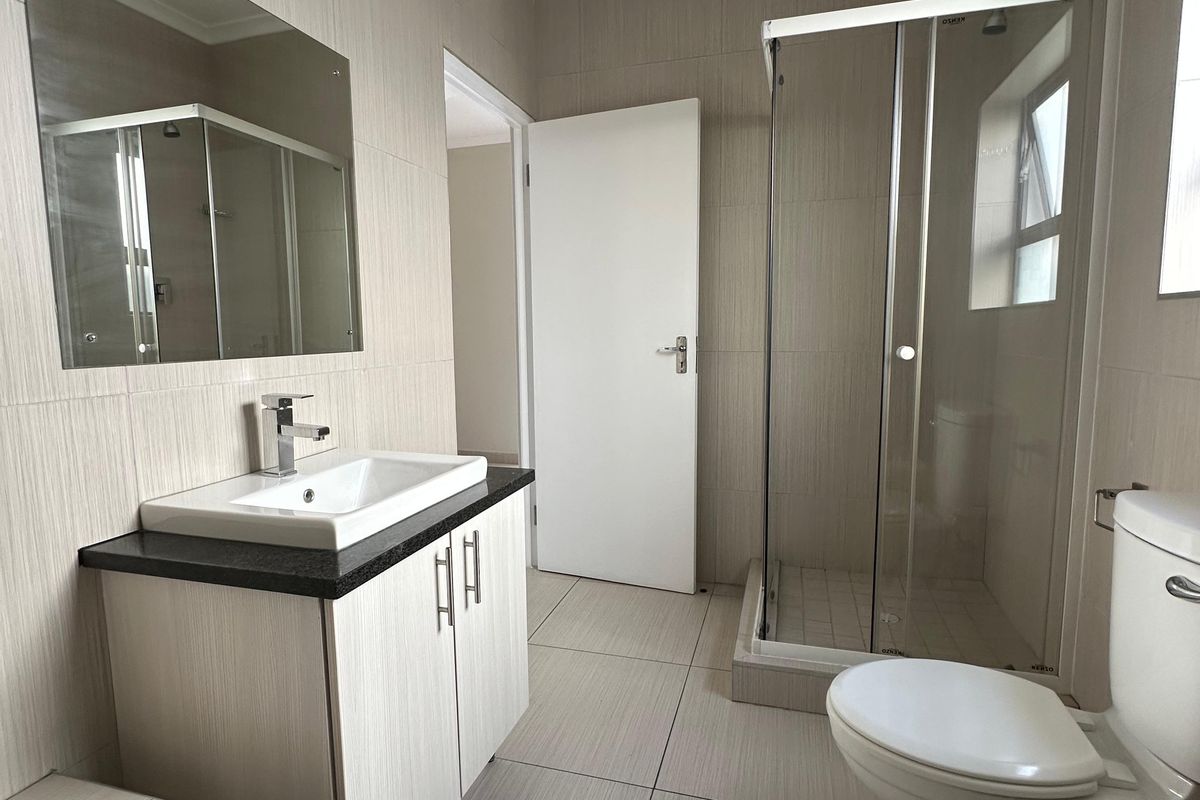 A clean, modern bathroom featuring a vanity with basin, a separate shower enclosure, a toilet, and a bathtub with neutral wall and floor tiling.