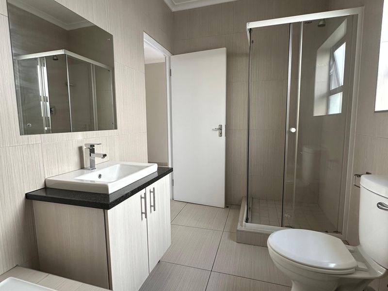 A clean, modern bathroom featuring a vanity with basin, a separate shower enclosure, a toilet, and a bathtub with neutral wall and floor tiling.