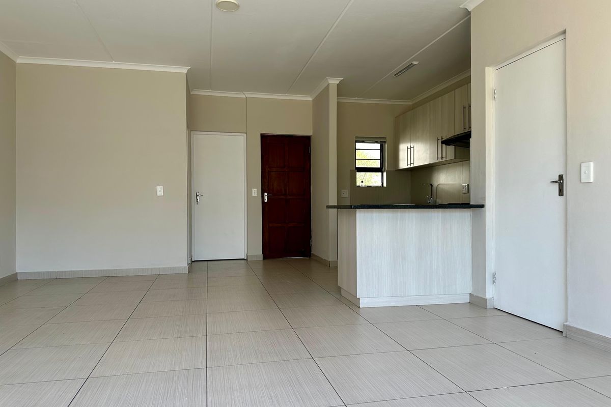An open-plan living and kitchen area featuring neutral tiled flooring, modern cabinetry, and a breakfast bar, presented in a clean, vacant condition.