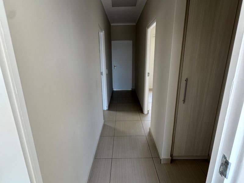A clean, well-maintained hallway featuring neutral tiled flooring and built-in storage cupboards, providing access to multiple rooms within the townhouse.