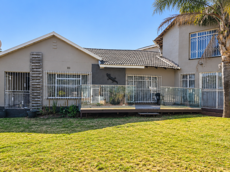 Rear view of the house featuring a raised timber deck with glass balustrade, tiled roof, and security bars on windows.