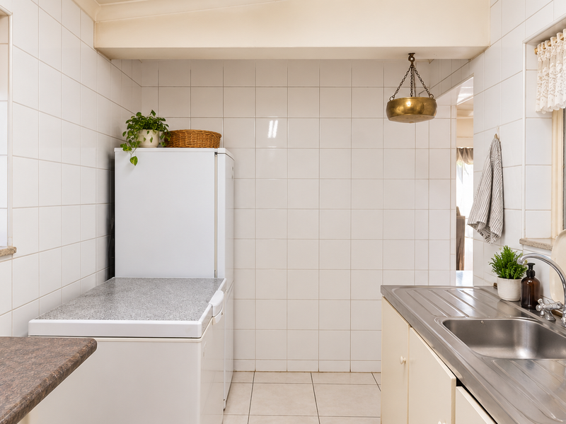 A functional laundry room featuring tiled walls, a stainless steel sink, and ample counter space, offering a clean and practical utility area.