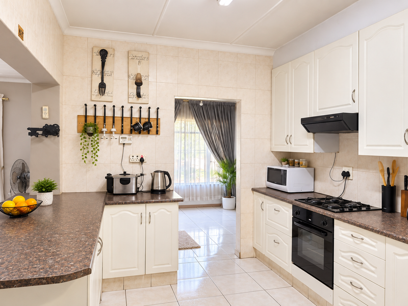 A well-maintained kitchen featuring white cabinetry, laminate countertops, a gas hob, and an integrated oven, with an open-plan layout connecting to the living area.