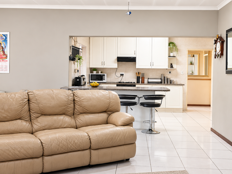 An open-plan living area featuring a functional kitchen with built-in cabinetry, a breakfast island, and neutral ceramic tile flooring throughout.