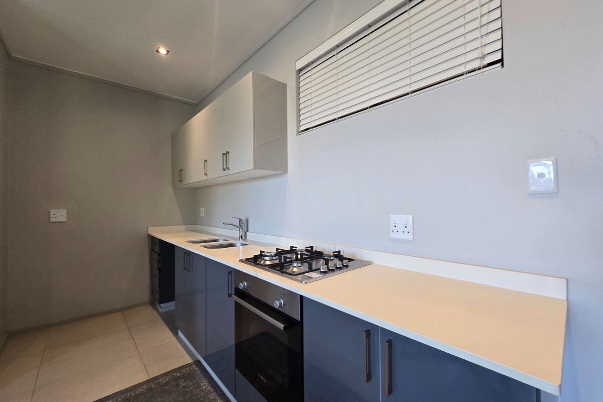 A modern, clean kitchen featuring dark grey lower cabinets, white upper cabinetry, a gas hob, built-in oven, and neutral countertops.