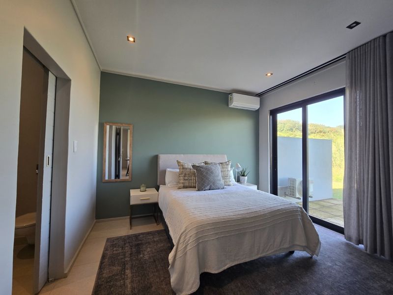 A modern bedroom featuring a sage green accent wall, split-system air conditioning, and large sliding glass doors providing access to an outdoor area.