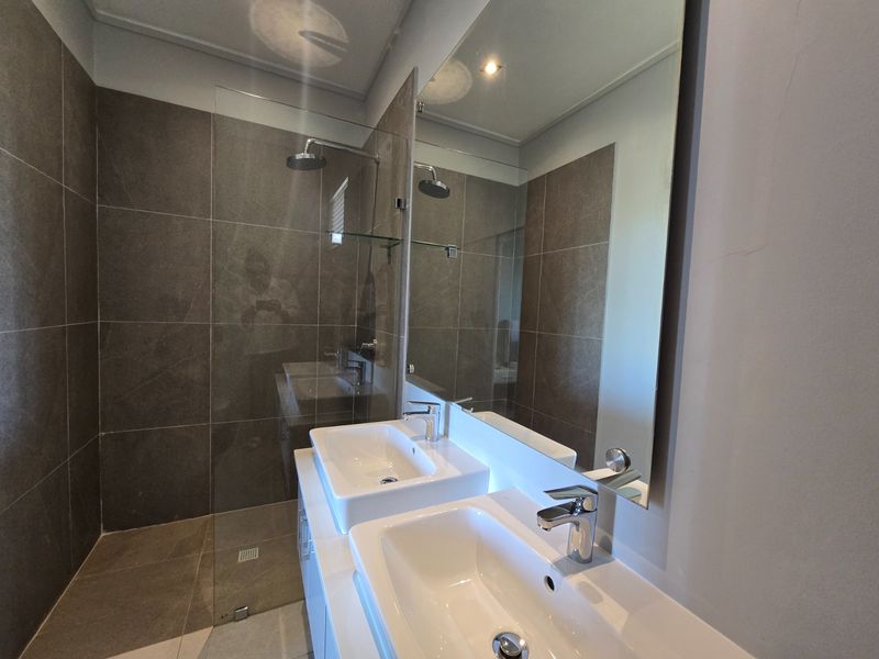 Modern bathroom featuring a double vanity with white basins, a spacious walk-in shower with a rain shower head, and large-format dark porcelain tiling.