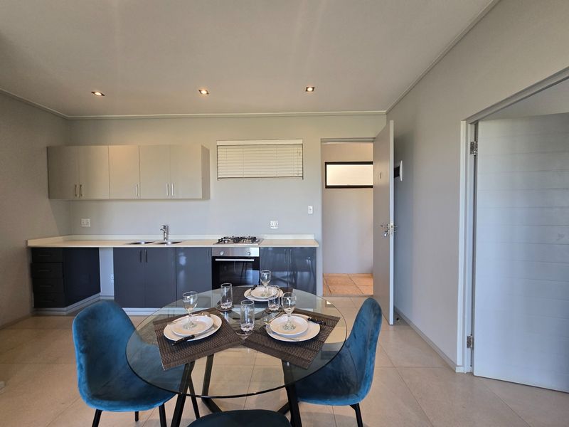 Modern open-plan kitchen and dining area featuring sleek cabinetry, built-in gas hob, under-counter oven, and neutral tiled flooring.