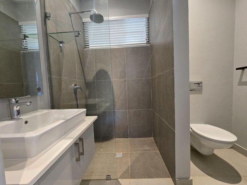 Modern bathroom featuring a walk-in shower with glass screen, wall-mounted toilet, and a sleek vanity unit with a ceramic basin.