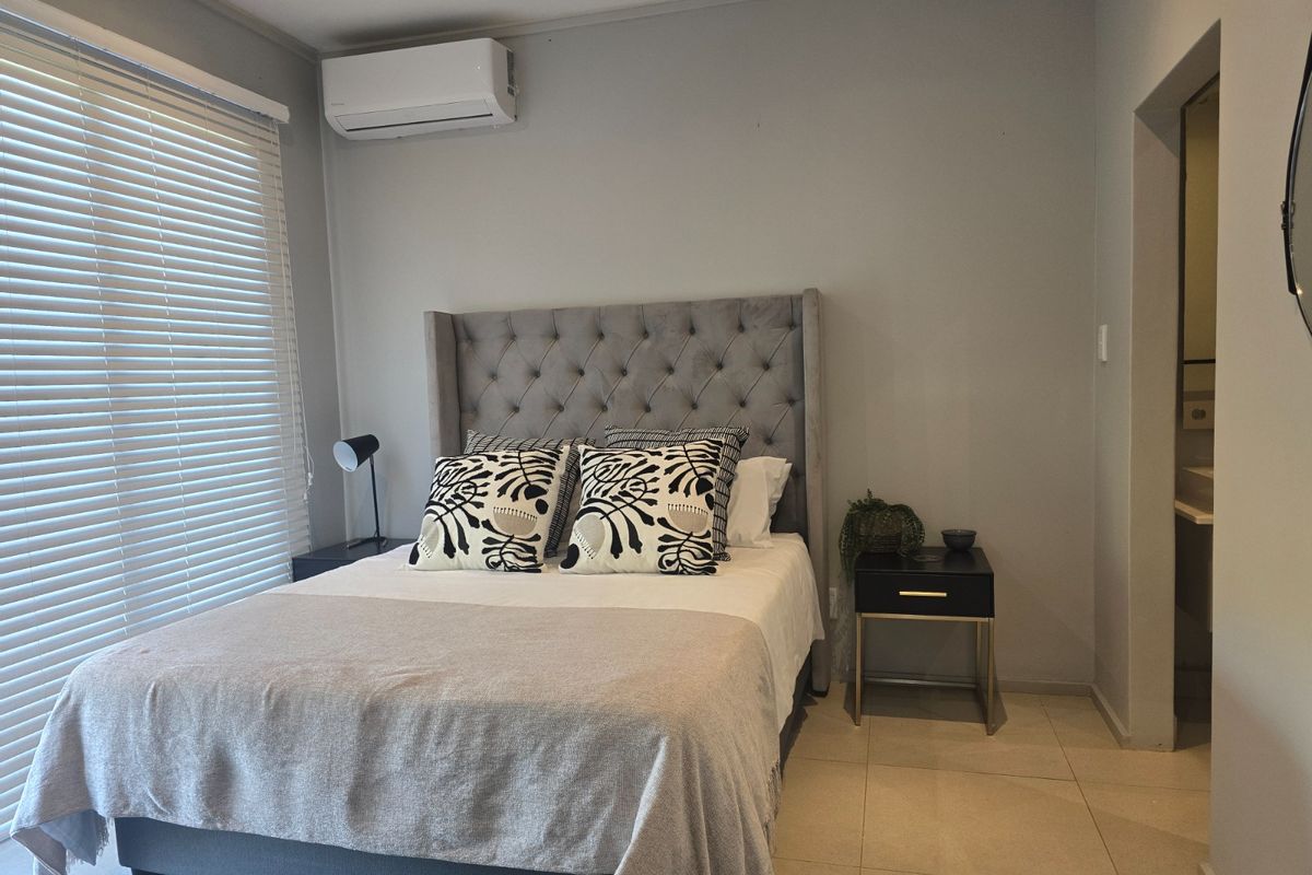 A well-maintained bedroom featuring tiled flooring, a wall-mounted split-system air conditioner, and venetian blinds, with an adjacent en-suite bathroom entrance.