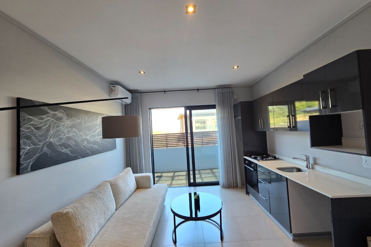 Modern open-plan living area featuring a sleek kitchen with dark cabinetry, stone countertops, and direct access to a private balcony.