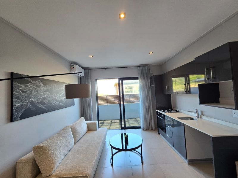 Modern open-plan living area featuring a sleek kitchen with dark cabinetry, stone countertops, and direct access to a private balcony.
