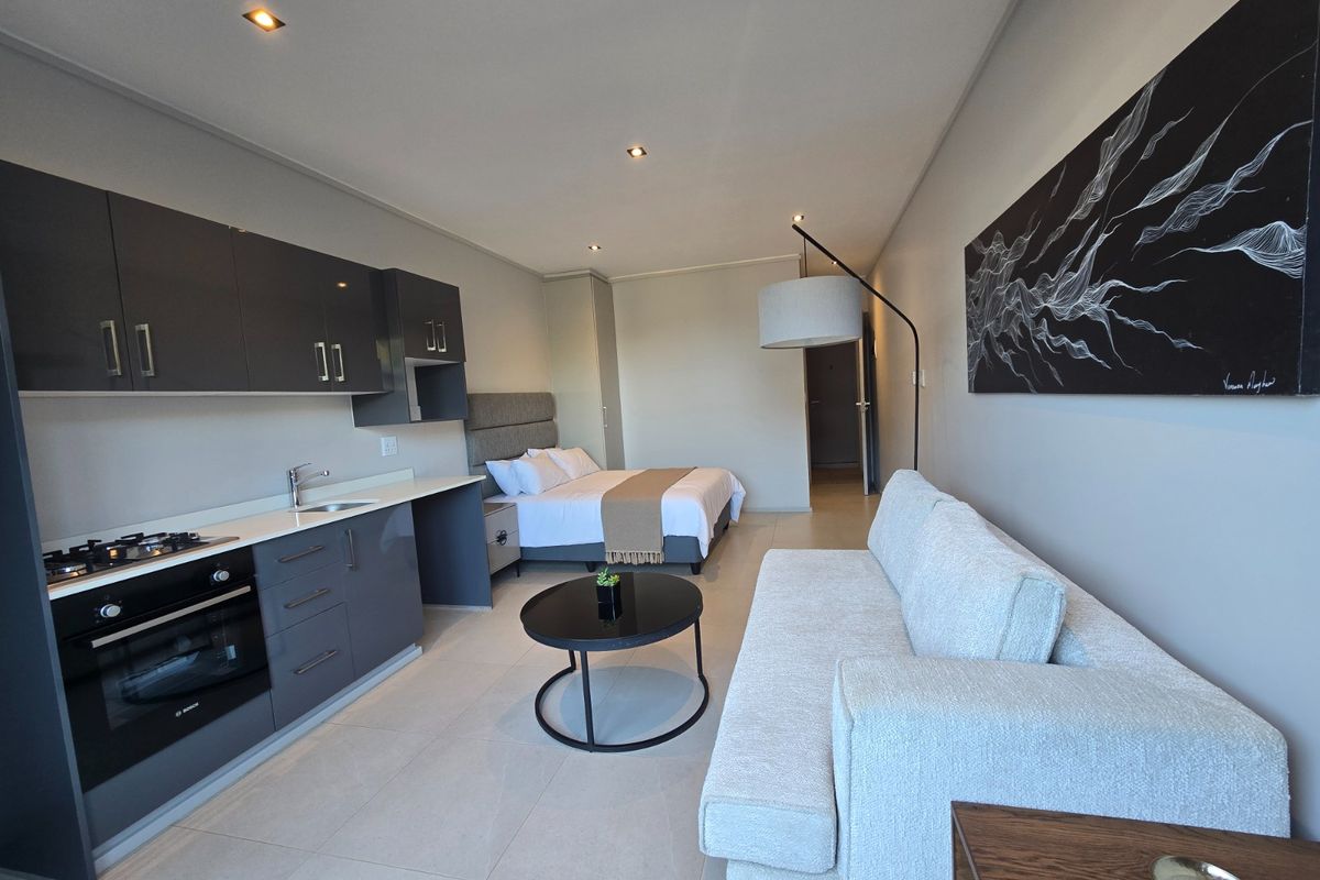 Modern open-plan studio apartment featuring a sleek kitchen with built-in appliances, tiled flooring, recessed lighting, and a combined living and sleeping area.