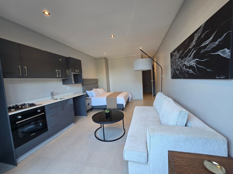 Modern open-plan studio apartment featuring a sleek kitchen with built-in appliances, tiled flooring, recessed lighting, and a combined living and sleeping area.