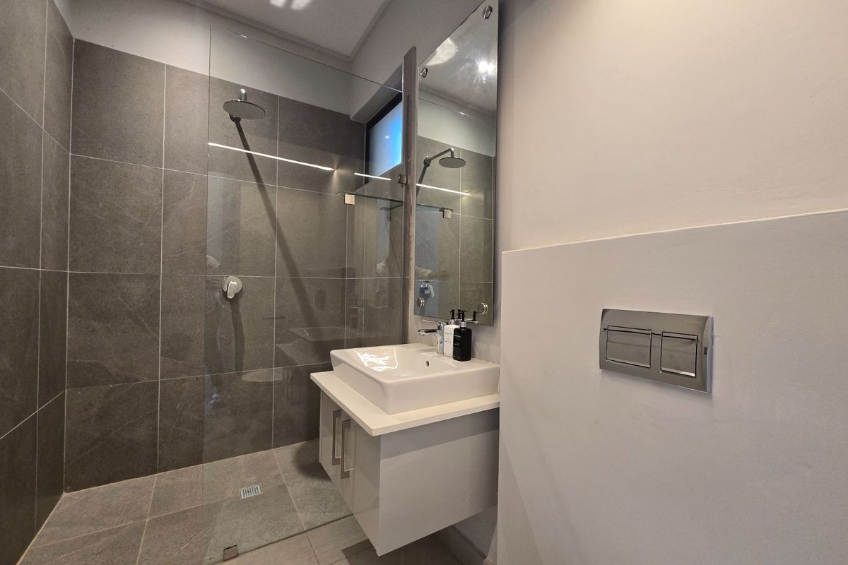 Modern bathroom featuring a walk-in shower with glass screen, wall-mounted vanity with basin, and contemporary tiled finishes.