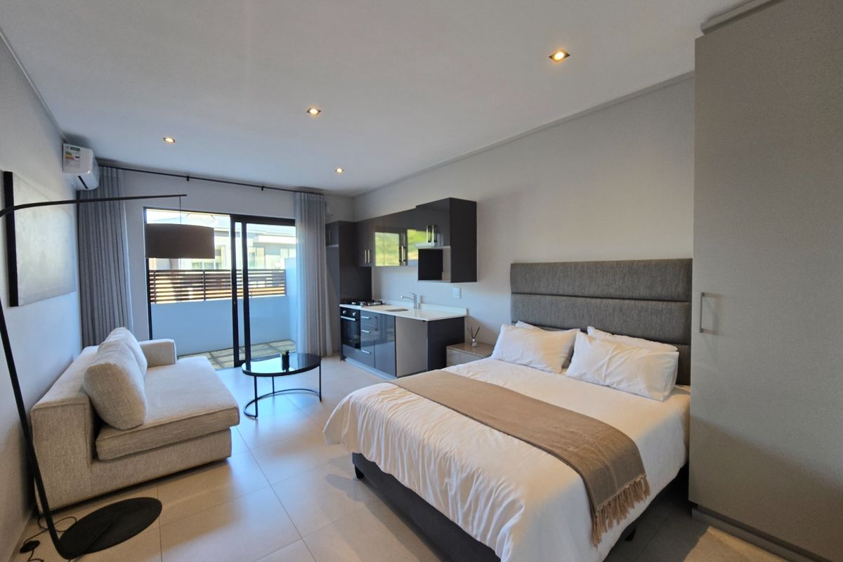 Modern open-plan studio apartment featuring a compact kitchenette, built-in wardrobe, and direct access to a private balcony through sliding glass doors.
