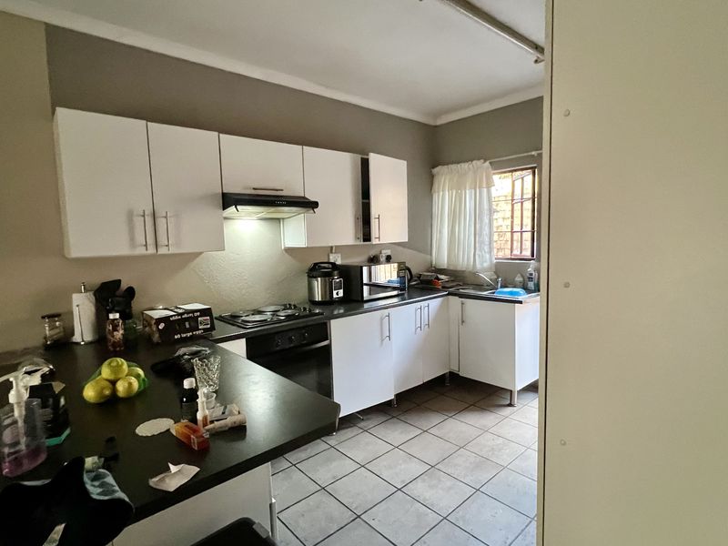A functional kitchen featuring white cabinetry, dark laminate countertops, an electric hob with extractor fan, and tiled flooring.