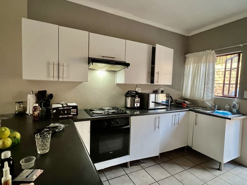 A functional kitchen featuring white cabinetry, dark countertops, an integrated oven and hob, and tiled flooring with direct access to an outdoor area.