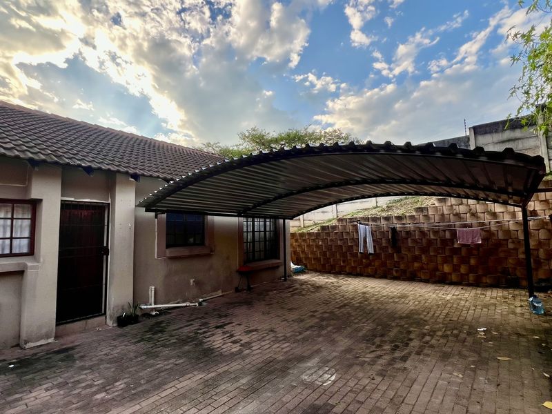 Rear exterior area featuring a covered carport, paved driveway, and a tiered retaining wall structure.