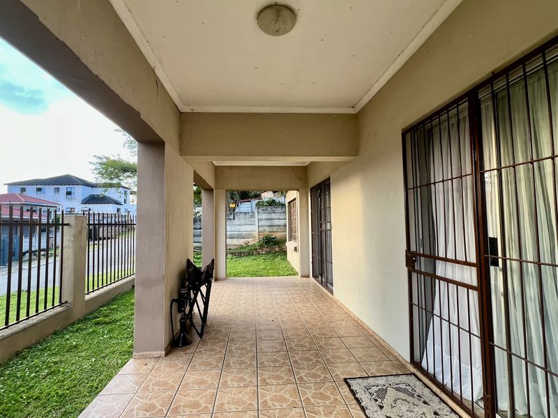A covered outdoor patio featuring tiled flooring, security gates, and sliding glass doors, providing a functional transition space between the interior and the garden.