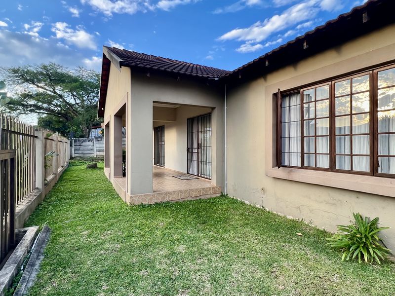 Rear view of the property featuring a covered patio, lawn area, and metal perimeter fencing.