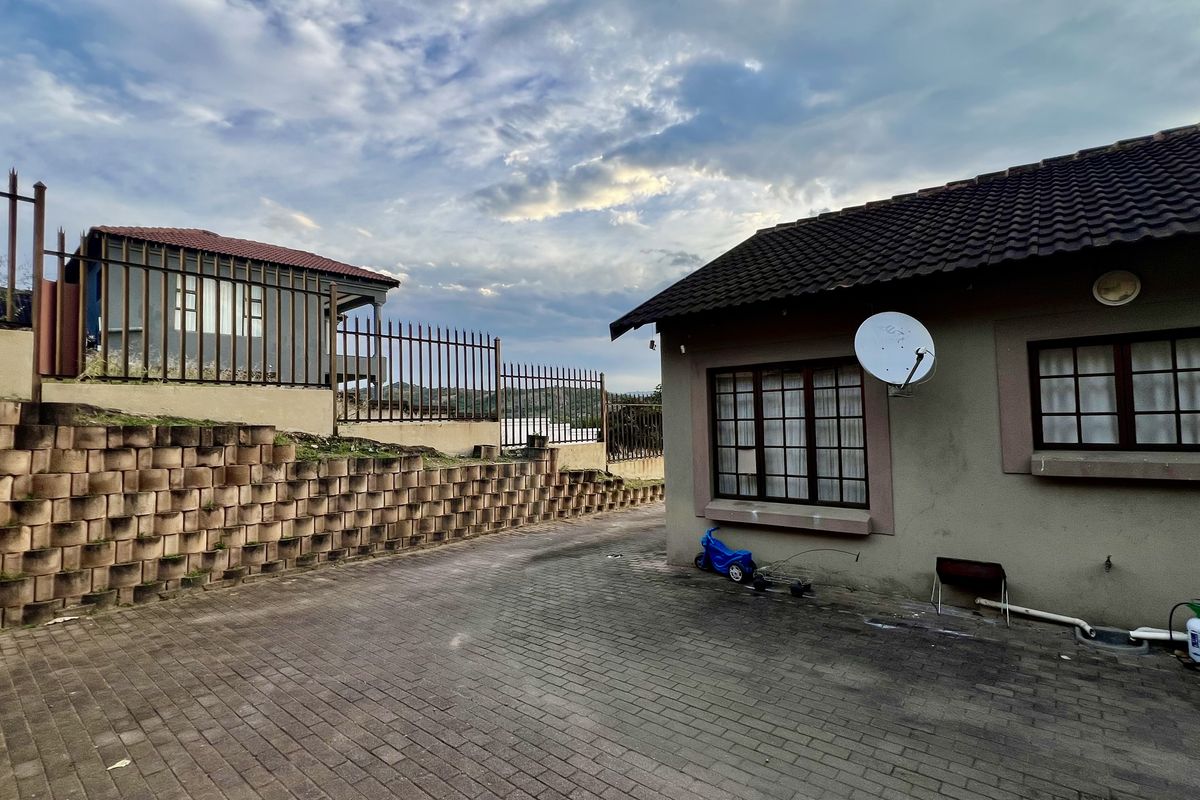 Rear exterior view of the property featuring a paved driveway, retaining wall, and security fencing surrounding the building structure.