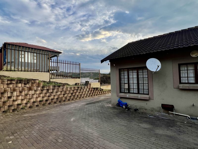 Rear exterior view of the property featuring a paved driveway, retaining wall, and security fencing surrounding the building structure.