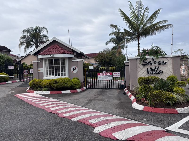 The entrance to Saxon Villa estate featuring a security gate, guard house, and paved driveway with speed bump.